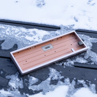 Outdoor lifestyle shot of the WOBKEY ZEN 65 Copper custom keyboard resting in a snowy winter setting